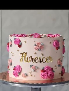 a white cake with pink flowers and gold lettering that says florescr on it