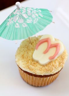 cupcake with frosting and an umbrella on it sitting on a table next to another cupcake