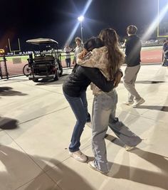 two women hugging each other on a baseball field at night with people in the background