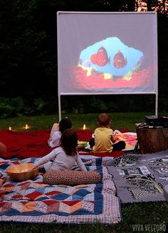 people sitting on blankets watching a movie in the park at night with candles lit up behind them