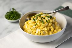 a white bowl filled with scrambled eggs and garnished with green herbs next to a spoon