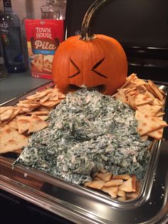 a pumpkin sitting on top of a metal tray filled with cheese and spinach chips