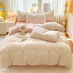 a bed with pink and white comforters in a bedroom next to a window filled with curtains