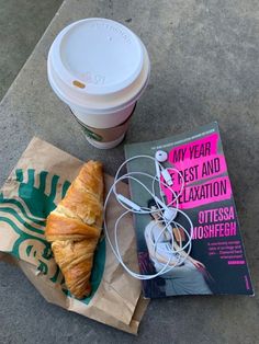 there is a croissant and a book on the ground next to a cup of coffee