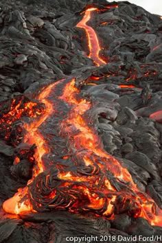 lava flowing down the side of a mountain covered in red and black rocks, as seen from above