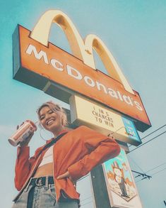 a woman standing under a mcdonald's sign holding a drink in her right hand