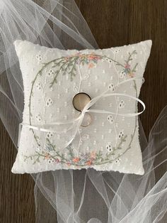 a white pillow with a ring on it sitting on top of a wooden table next to tulle