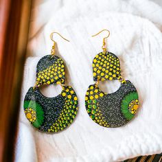 a pair of green and yellow earrings sitting on top of a white cloth covered table