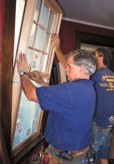 two men in blue shirts are working on a window