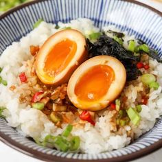 two boiled eggs on top of rice in a blue and white bowl with chopsticks