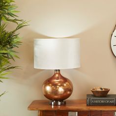 a lamp sitting on top of a wooden table next to a clock and plant in a vase