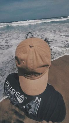 a person wearing a hat sitting on top of a sandy beach next to the ocean