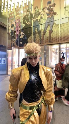 a man dressed in costume walking down a street next to a tall glass wall with anime characters on it