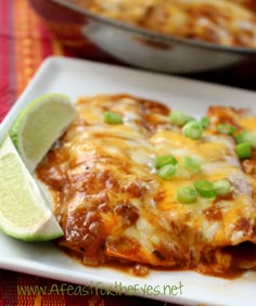 a white plate topped with enchilada covered in cheese and green onions next to a lime wedge