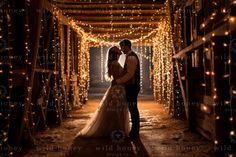 a bride and groom standing in an open barn doorway with fairy lights on the ceiling