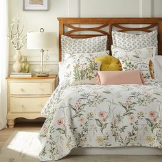 a bed with floral comforter and pillows on top of it, next to a night stand