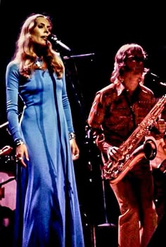 a woman in a blue dress standing next to a man with a saxophone on stage