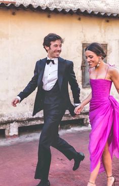 a man in a tuxedo and a woman in a purple dress are holding hands