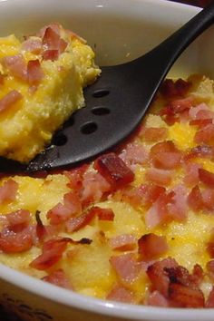 there is a spoon in a bowl with eggs and bacon on it, ready to be eaten