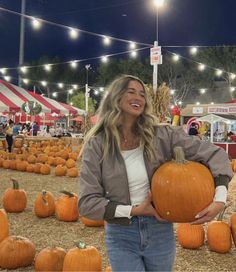 a woman holding a large pumpkin in front of many other pumpkins on the ground