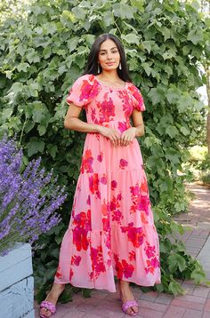 a woman standing in front of a bush wearing a pink dress with flowers on it