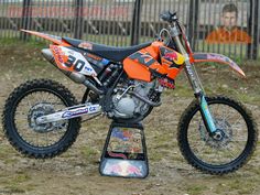 an orange dirt bike parked on top of a metal stand in front of a fence