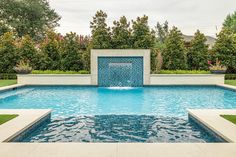 a pool with a fountain in the middle of it surrounded by grass and trees,