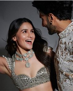 a man standing next to a woman in a silver bra top and matching necklaces