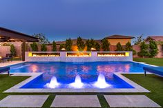 an outdoor swimming pool surrounded by grass and fire pit with seating around it at dusk