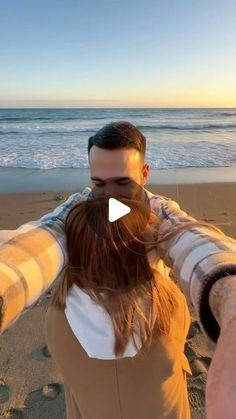 a man and woman standing on top of a beach next to the ocean with their arms around each other