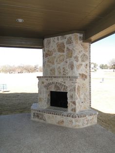 a stone fireplace in the middle of a covered area with grass and trees behind it