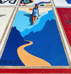 a woman sitting on the ground in front of a mural with mountains and rivers painted on it