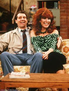 a man and woman sitting on a couch in front of a coffee table, smiling