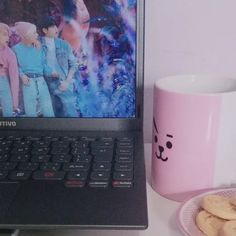 a laptop computer sitting on top of a desk next to a plate of cookies and a mug