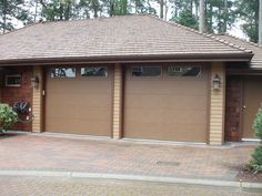 two garages in front of a brick driveway with trees and bushes around them on either side