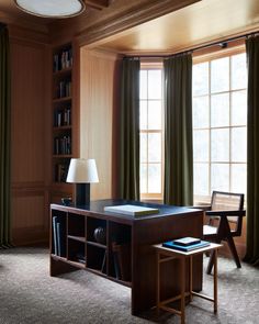 a room with a desk, chair and bookshelf next to a large window