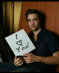 a man sitting on a bed holding a sign with the words i love you written on it