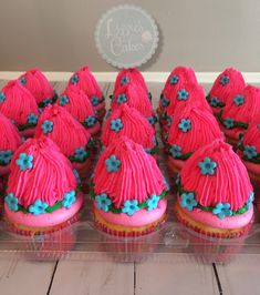 cupcakes with pink frosting and blue flowers on top are arranged in rows