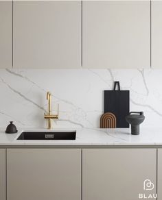 a white kitchen with marble counter tops and gold faucets on the sink area