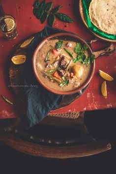 a bowl of soup with meat and vegetables on a table next to some pita bread