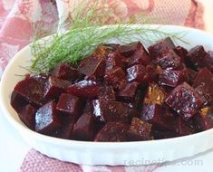 a white bowl filled with cooked beets on top of a pink table cloth next to a green sprig