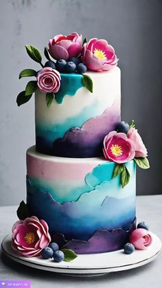 a three tiered cake with flowers on the top and bottom layer is painted in blue, pink and purple