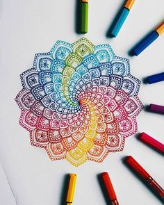 colored crayons and markers are arranged around an intricately designed design on paper