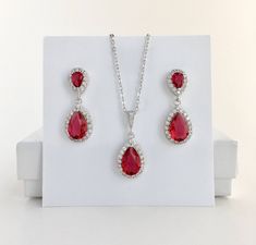 Super sparkly red ruby rhodium plated cubic zirconia bridal set includes : # Earrings feature a teardrop with pear cut red ruby cubic zirconia center surrounded by tiny round zirconia crystals. Teardrop dangles from red ruby cubic zirconia teardrop ear stud. Total length of the earrings is 2.9 cms. #Necklace pendant featuring a teardrop with pear cut ruby cubic zirconia center surrounded by tiny round zirconia crystals and dangles from cubic zirconia bail. Length of the rhodium plated chain is 1 Red Cubic Zirconia Jewelry Sets For Weddings, Red Sparkling Stones Jewelry Sets For Wedding, Red Sterling Silver Jewelry Sets For Wedding, Red Sterling Silver Wedding Jewelry Sets, Ruby Red Wedding, Ruby Jewelry Set, Red Crystal Jewelry, Gold Bridesmaid Jewelry, Red Ruby Earrings