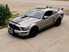 a silver car parked on top of a cement parking lot next to a green bush