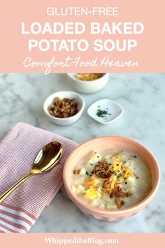 a bowl of loaded baked potato soup on a marble countertop with two spoons