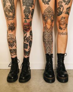 two women with tattoos on their legs standing next to each other, both wearing black combat boots