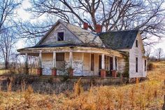 an old run down house sitting in the middle of a field with no leaves on it