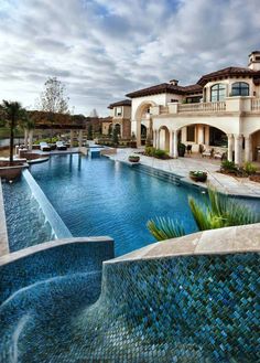 an outdoor swimming pool with blue tiles and palm trees in the foreground, next to a large house