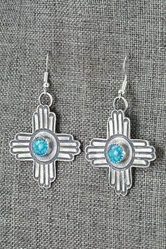 These turquoise and sterling silver New Mexico Zia symbol shaped earrings were made by Navajo silversmith Kevin Billah. The backs are signed KB and stamped sterling.Length: 2 1/4"Width: 1 3/8"Free shipping on all orders! We ship with USPS and always include tracking. All orders ship within a day of payment.Returns are accepted up to 30 days after you receive your order. Just send us a message. Our shop offers cash back or store credit. The item must be returned in new condition. Turquoise Concho Dangle Jewelry, Blue Concho Dangle Earrings, Artisan Turquoise Pierced Jewelry, Traditional Turquoise Sterling Silver Earrings, Traditional Turquoise Jewelry With Concho, Traditional Turquoise Concho Jewelry, Traditional Concho Earrings For Gift, Traditional Concho Earrings As Gift, Turquoise Nickel-free Southwestern Earrings